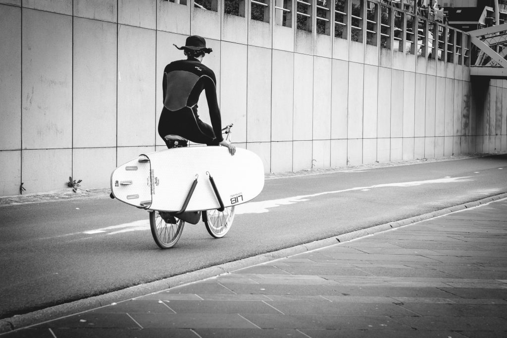 Surfer biking with his surfboard on the side. Black and white